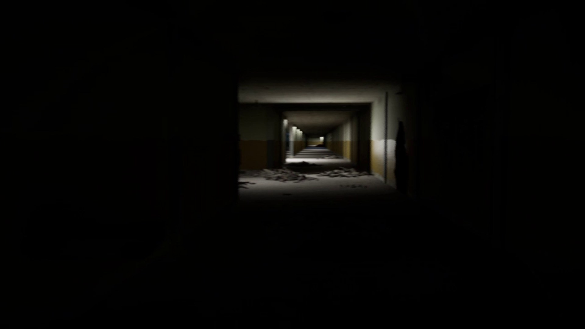 A pitch-black corridor with one small lit doorway far ahead