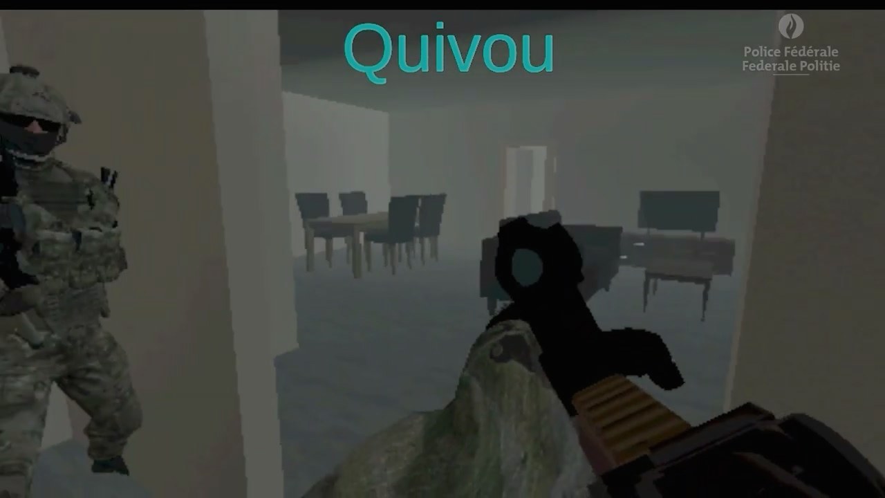 A first-person view inside the simulated house: a wall in the middle of the frame, a teammate to the left of it and an open doorway into the next room